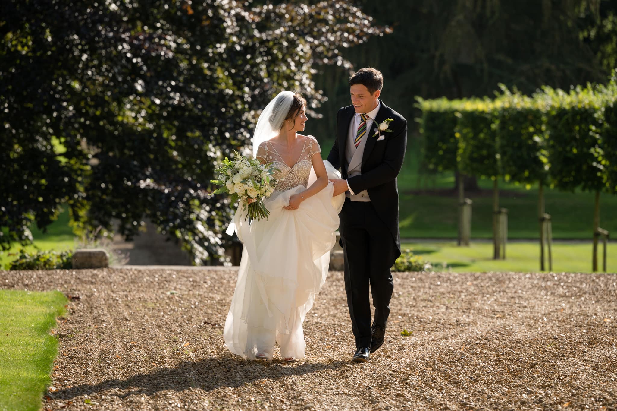 Groom carrying bride's train as she walks